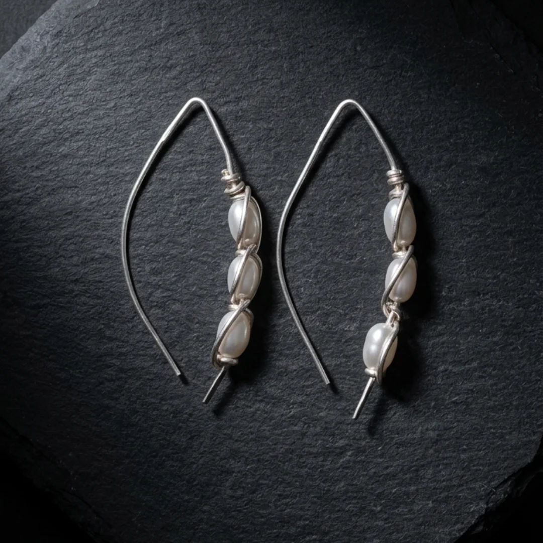 Foto 1 (producto sobre pizarra): Wire wrapped pearl earrings by REPIOR® — three oval freshwater pearls per earring in silver-plated copper cage, 5cm drop Foto 2 (detalle de cage): Close-up of handmade wire wrapped pearl earring cage — silver-plated copper wire formed around oval freshwater pearl Foto 3 (par completo): Cage Pearl Cascade earrings by REPIOR® — set of 2, six freshwater pearls in wire cage, handcrafted in England Foto 4 (AI visual): Wire wrapped pearl earrings worn — long marquise drop earring with pearl cage, REPIOR® handmade jewellery England